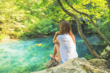 Young woman sitting near the beautiful lake in nature.