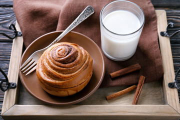 Plate with sweet cinnamon roll and glass of milk on wooden tray