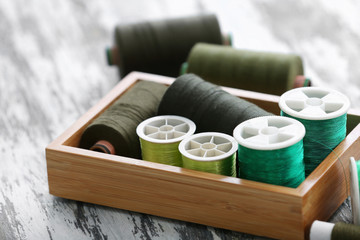 Fototapeta na wymiar Composition with green sewing threads in box on wooden table