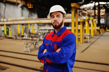 Cute young worker in a white construction helmet against a background of a factory or production