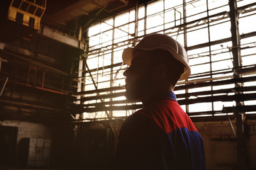Fototapeta na wymiar Silhouette of a worker in a construction helmet against a background of a factory or production