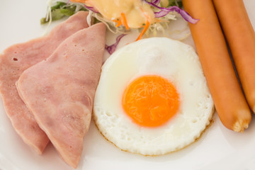 Breakfast with egg, ham, sausage in White dish on wood table