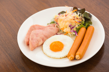 Breakfast with egg, ham, sausage in White dish on wood table