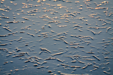 Nature background of freezing cracked water surface with reflection of sunlight.
