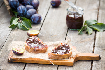 Sandwich with plum jam on old wooden table in garden.