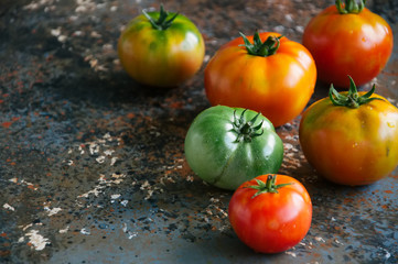 Different sizes and colors of fresh tomatoes on a rusty background. Top view and copy space.