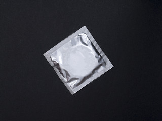 Silver Condom in package on black background.