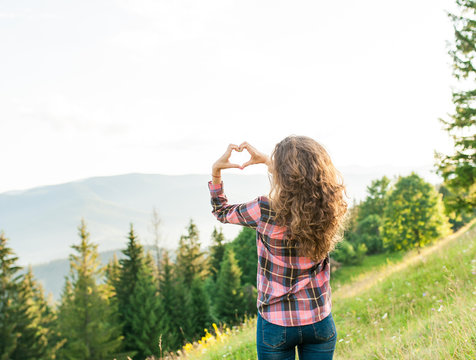 Girl making a heart-shape with mountain landscape in the background.