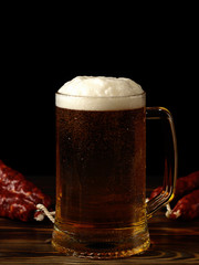 A pint of light beer and sausage on a wooden table.