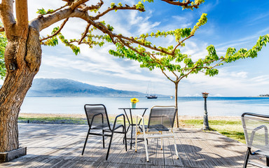 Street outdoor cafe on Embankment of Corinth Gulf beneath the tree. View at solitary vessel on horizon. Beautiful sea view on breathtaking vista, amazing spring scenery. Fresh blue sky over scene.