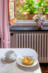 Daylight view to pancakes with syrup and a white cup on table. Window and flower background.