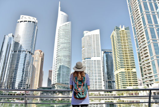 Happy young traveler woman in big city Dubai in hat and travel bag