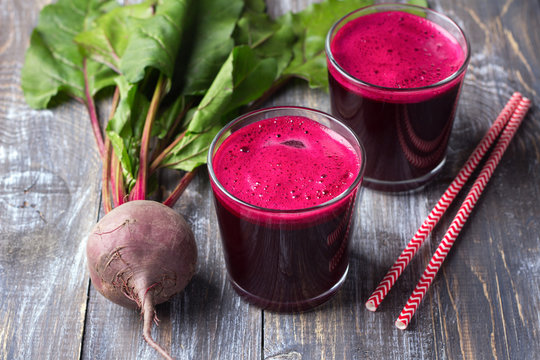 Fresh beet juice in glasses with a straw on a wooden background, selective focus. Healthy detox diet