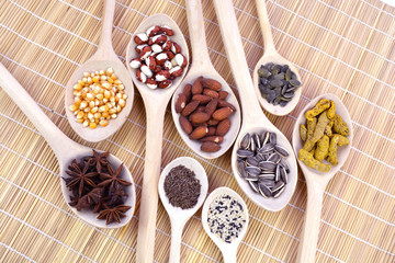 wooden spoons on bamboo mat with seeds, nuts and spices