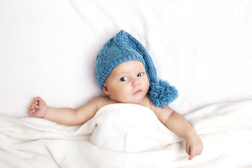 baby boy lying in bed, in blue cap
