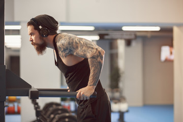 Attractive young adult man doing dips exercise in modern fitness center. Toned image.