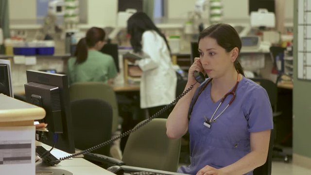 Nurses answers phone in busy nurse's station in a modern hospital.