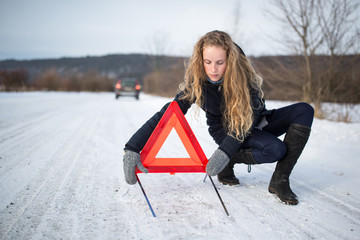 Young woman setting up a warning triangle and calling for assistance after her car broke down in...