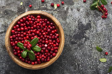 Red lingonberry in wooden bowl on rustic surface, top view