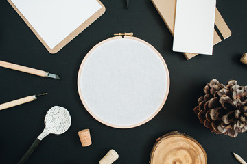 Embroidery frame, clipboard, handmade spoon, cone on black chalk board background. Top view, flat lay hipster workspace concept.