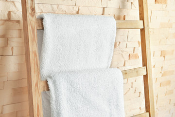 Fototapeta na wymiar Ladder with soft towels near brick wall