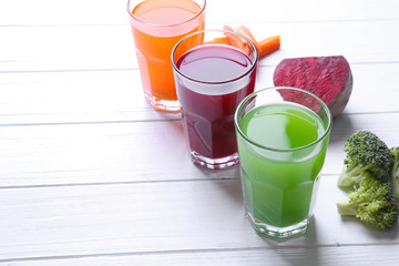 Fresh vegetable juices in glasses and ingredients on wooden table