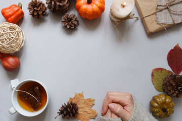 Autumn background. Female hands, cup of tea, autumn decoration on gray background.
