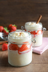 Creamy rice pudding with strawberry in jar on wooden table