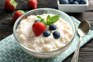 Creamy rice pudding with berries in bowl on wooden table