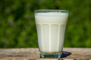 Glass of milk on wooden table with nature background