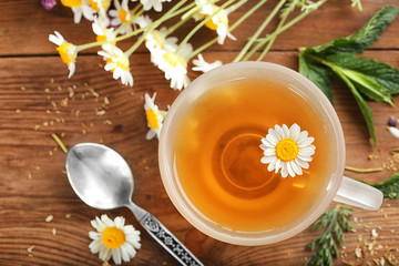 Cup of herbal tea and chamomile flowers on wooden table