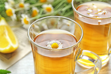 Cups of herbal tea and chamomile flowers on table, closeup
