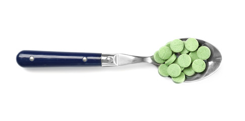 Spoon with chlorella tablets on white background