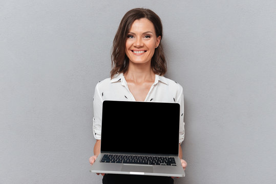 Happy woman in business clothes showing blank laptop computer screen