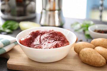 Piece of raw meat in bowl and potatoes on wooden board