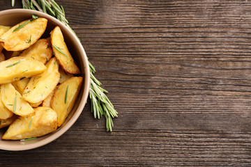 Bowl with delicious baked potato wedges on wooden background