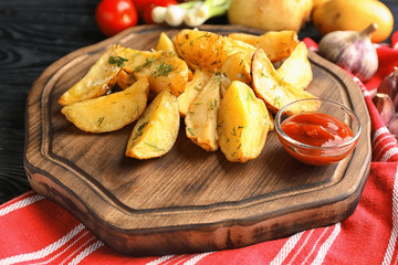 Wooden board with delicious baked potato wedges and sauce on table