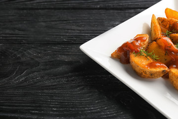 Plate with delicious baked potato wedges and sauce on wooden background