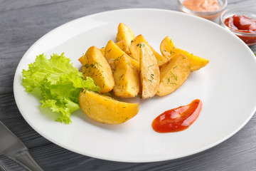 Plate with delicious baked potato wedges and sauce on table