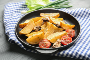 Frying pan with delicious baked potato wedges on napkin