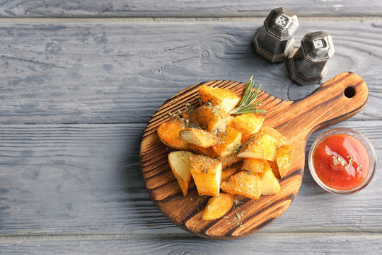 Wooden board with delicious baked potato wedges and sauce on table