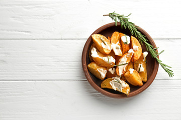 Bowl with delicious baked potato wedges on wooden background