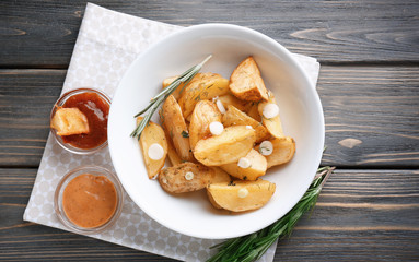 Plate with delicious baked potato wedges and sauce on table
