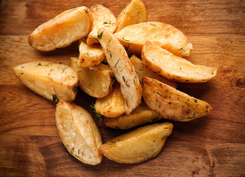 Delicious baked potato wedges on wooden background