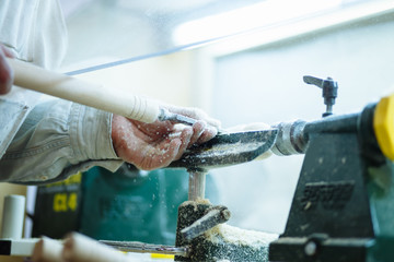 hands hold chisel near lathe, an artisan carves piece of wood using manual lathe