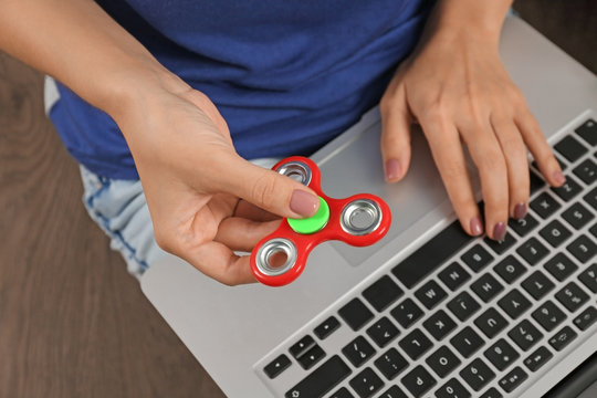 Woman rolling modern spinner and using laptop indoors