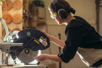 Attractive female carpenter using some power tools for her work in a woodshop