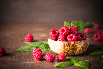 Fresh raspberries in wooden bowl on white table.