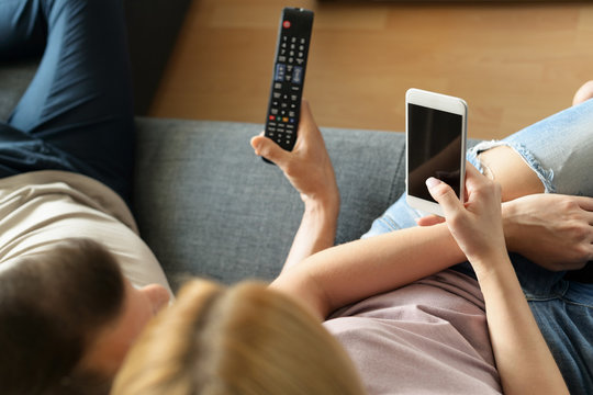 Young unrecognisable couple at home, watching television and texting
