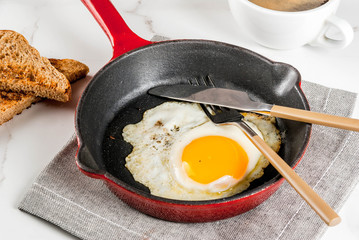 Breakfast with toasted bread, fried egg on iron pan and coffee on white marble background copy space